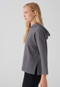 Felpa grigia con cappuccio realizzata in tessuto morbido, caratterizzata da un fit rilassato, maniche lunghe e spacco sui lati dell'orlo per un comfort aggiuntivo.