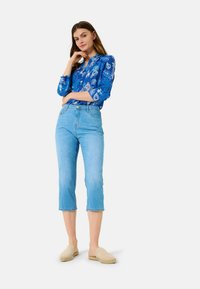 Blusa a maniche lunghe blu con motivo paisley bianco, abbinata a jeans cropped blu chiaro e scarpe slip-on beige.