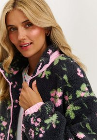 Fleeceová bunda s tmavosivým telom, ružovým kvetinovým vzorom a svetloružovými lemami. Obsahuje zips a rebrované manžety, ponúkajúce mäkkú textúru.