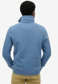 Sudadera de forro polar azul con cuello alto, puños y dobladillo acanalados, textura suave y diseño sencillo. Sin logotipos ni patrones visibles.