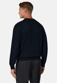 Marineblauwe geribbelde gebreide trui met lange mouwen, ronde hals en afgewerkte manchetten, gecombineerd met donkergrijze broek, die een gestructureerd oppervlak toont.