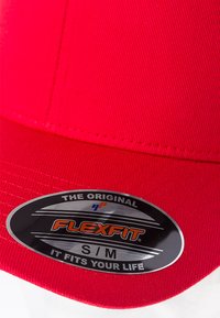 Crvena kapa s ravnim obodom, izrađena od teksturiranog materijala. Sadrži srebrnu ovalnu oznaku s natpisom "FLEXFIT" i veličinom "S/M." Čist, jednostavan dizajn.