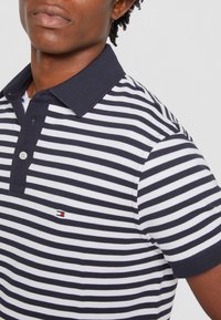 Mørkeblå og hvid stribet polo shirt med krave, der har en knaplukning foran og et lille mærke-logo på brystet.