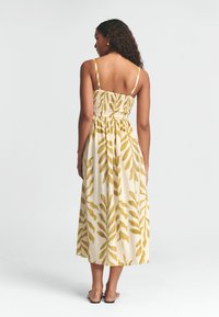 Kollane lehemustritega midi kleit, millel on kokku volditud seljaosa ja õhukesed rihmad, valminud kergest kangast mugavuse tagamiseks.