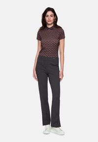 Kurzes, eng anliegendes Poloshirt mit geometrischem Muster in dunklem Weinrot und Creme; kombiniert mit maßgeschneiderten schwarzen Hosen und weißen Turnschuhen.