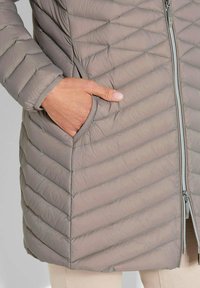 Gequilted grijze pufferjack met verticale kanalen, ritssluiting en zijzakken. De stof lijkt glad en licht van gewicht.