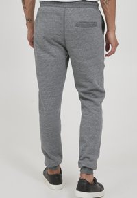 Grå tapered joggebukser i teksturert stoff, med elastisk liv og en baklomme. Kombinert med svarte sneakers, gir et avslappet uttrykk.