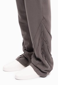 Grijze joggingbroek met een gestructureerd zijpaneelontwerp en gelaagde stofaccenten. Gecombineerd met witte schoenen met een gladde zool.