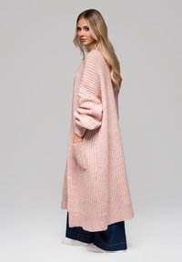 Dlouhý cardigan s otevřeným předním dílem v jemně růžové barvě, pletená textura, s velkými rukávy a bočními kapsami, doplněný širokými džíny.
