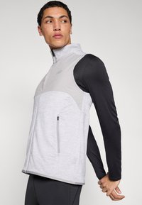 Graue und schwarze athletische Weste mit durchgehendem Reißverschluss, hohem Kragen und Tasche, mit strukturiertem Stoff und figurbetontem Design für sportliche Aktivitäten.