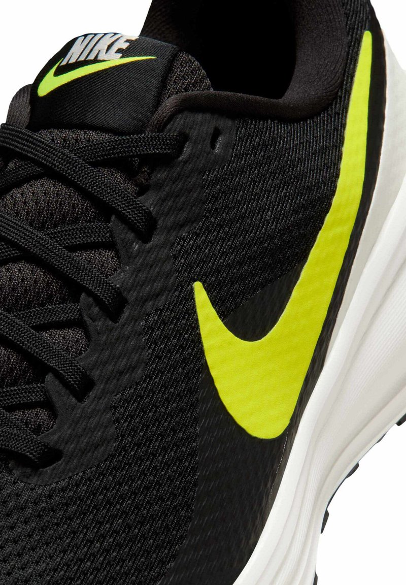 Zapatilla deportiva negra con parte superior texturizada, logo de Nike en color amarillo brillante, cordones negros y una entresuela blanca con forma curva.