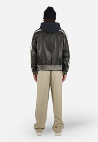 Zwarte leren bomberjack met verticale naden, gestreepte zoom, en een marineblauwe hoodie eronder. Beige ontspannen pasvorm broek.