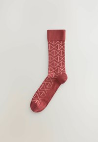 Chaussette rouge à motif, avec une bordure côtelée, arborant un design géométrique en blanc. Fabriquée en matériau textile doux, idéale pour une tenue décontractée.