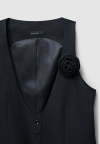 Schwarzes ärmelloses Kleid mit tiefem V-Ausschnitt, satinierter Innenfutter, fünf vorderen Knöpfen und einem Stoffblumenakzent auf der linken Seite. Marke: Calliope.