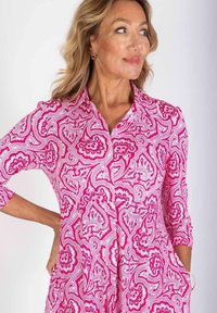 Różowa sukienka w wzór paisley z rękawami o długości trzech kwart, z zapięciem na guziki z przodu i kieszeniami. Tkanina ma lekką, gładką teksturę.