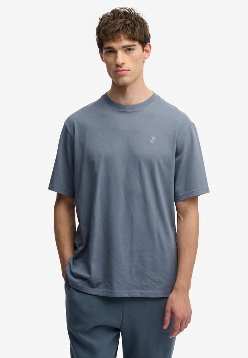 Camiseta de algodón azul claro con cuello redondo, mangas cortas y un sutil bordado del logo en el pecho, combinada con pantalones a juego.