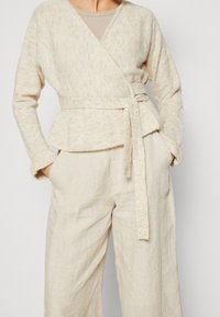 Light beige wrap sweater in soft, textured knit with a tied waist. Paired with loose, light beige linen trousers. Casual design, minimal detailing.