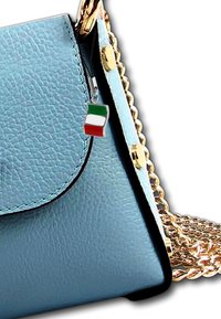 Sac en cuir texturé bleu avec une chaîne dorée et un petit charme en forme de drapeau italien. Il présente une fermeture à rabat avec des coutures noires.