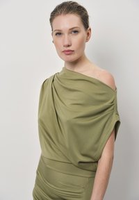 Olijf groene gedrapeerde jurk met een off-shoulder ontwerp, voorzien van een zachte textuur en een strakke corsage met gedetailleerde plooien en accent aan de zijkant.