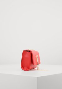 Borsa a mano in pelle rossa con superficie texture, forma quadrata, hardware dorato e tracolla a catena. Presenta una chiusura a pattina e una leggera lucentezza.