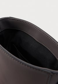 Primo piano dell'apertura di una borsa in pelle marrone scuro che mostra la fodera interna in tessuto nero e le cuciture dettagliate sul bordo.