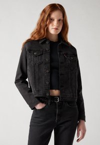 Giacca in denim nera con due tasche frontali, chiusura a bottoni e vestibilità corta. Tessuto testurizzato e dettagli di cucitura discreti.