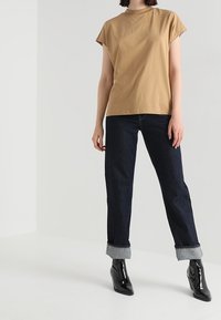 Camiseta de algodón beige de manga corta, combinada con jeans rectos de pierna oscura y puños arremangados, y botines de charol negros.