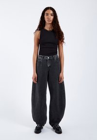 Svart ärmlös topp med hög halsringning; lösa, högmidjade, blekta svarta jeans; enhetlig textur; svarta skor; minimala accessoarer.