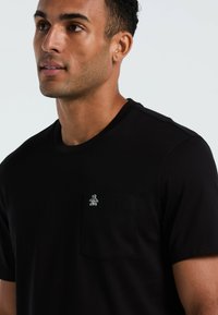 Zwarte katoenen t-shirt met een ronde halslijn en korte mouwen. Heeft een klein penguinlogo op de linkerkant van de borstzak en een zachte textuur.