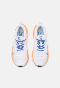 Weiße Sportschuhe mit orangefarbenen Akzenten, ausgestattet mit einer strukturierten Oberseite, blauen Schnürsenkeln und einer gepolsterten Zunge, entworfen für Leistung und Komfort.