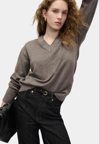 Pull col en V marron clair en matière douce, associé à un jean denim foncé taille haute. Le pull présente des poignets côtelés et une coupe décontractée.