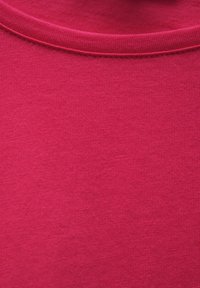 Tessuto di cotone fucsia con una texture liscia, caratterizzato da un collo rotondo e un bordo a coste al colletto. Materiale leggero e tessuto uniformemente intrecciato.