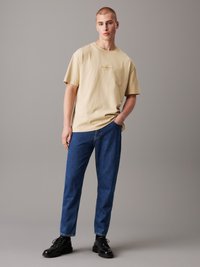 Ljusbeige oversized bomullströja med små broderade detaljer, kombinerad med mörkblå smala jeans och svarta snörboots.