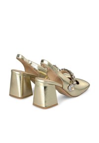 Zapatos de tacón de slingback metálicos dorados con punta afilada, tacón alto y grueso, adornados con pedrería decorativa a lo largo de la correa.