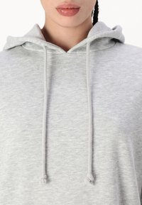 Siva dukserica s mekim tekstilom, s vezicom za podešavanje i okruglim izrezom. Tkanina izgleda lagano i ležerno.