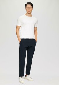 Weißes Baumwoll-T-Shirt, marineblaue Hose und weiße Sneaker. Das T-Shirt hat kurze Ärmel, und die Hose ist tapered mit einem sauberen Finish.