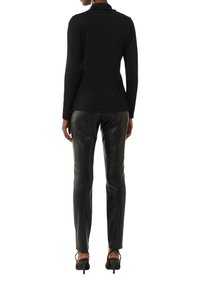 Zwarte top met lange mouwen en hoge hals, gecombineerd met zwarte leren broek. De broek heeft een gladde textuur en een getailleerde pasvorm. Zwarte hoge hakken.