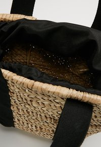 Borsa intrecciata in paglia con manici larghi in tessuto nero e rivestimento interno in tessuto nero, con apertura visibile.