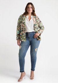 Floral blazer in green, pink, and blue, paired with a white button-up shirt, distressed blue jeans, and nude high-heeled sandals.