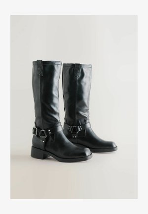 Svarta läderknähöga stövlar med en slät yta, spännen och en låg klack. Har dragloopar högst upp för enkel påtagning.