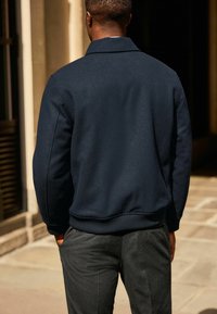 Marineblaues Sweatshirt mit lockerer Passform, mit einem Kragen und gerippten Bündchen. Kombiniert mit dunklen Hosen, die eine glatte Textur zeigen.