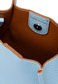 L'interno della borsa in pelle blu chiaro presenta una texture liscia e una fodera marrone. Include una chiusura a scatto e un'impronta "made in Italy".