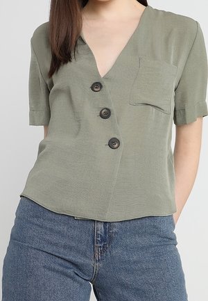 Olivgrünes Kurzarmblusenshirt mit V-Ausschnitt, drei schwarzen Knöpfen, einer Brusttasche und einem leicht gewellten Saum, aus einem weichen Stoff gefertigt.