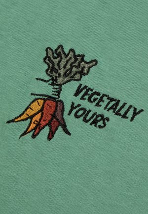Tissu en coton vert avec un motif brodé d'une carotte avec des feuilles, accompagné du texte "VEGETALLY YOURS" en fil noir.