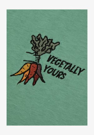 Tissu en coton vert avec un motif brodé d'une carotte avec des feuilles, accompagné du texte "VEGETALLY YOURS" en fil noir.