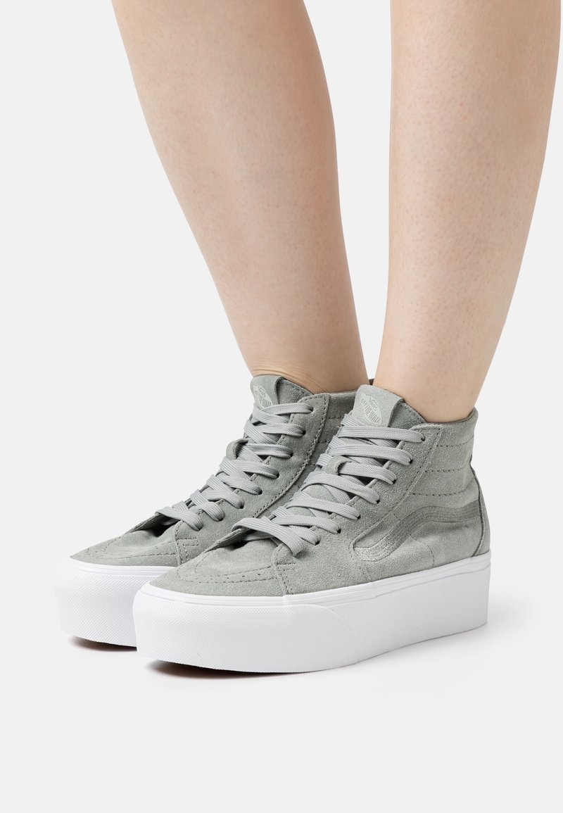 Baskets en daim gris montant à la cheville avec semelles plateformes blanches, portées sur jambes nues sur un fond pâle.