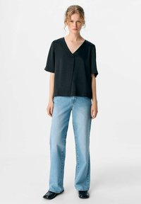 Schwarzes kurzärmliges Oberteil mit V-Ausschnitt, lockere Passform und leichtem Material, kombiniert mit hellblauen weiten Jeans und schwarzen Schuhen.