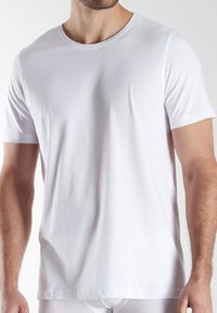 Man wearing a plain white short-sleeve crew neck t-shirt, shown from shoulders to hips against a plain background.