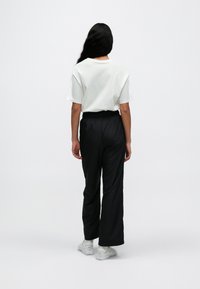 Λευκό t-shirt με κοντά μανίκια και μαύρο παντελόνι με ελαστική μέση, λείο ύφασμα, άνετη εφαρμογή, εμφανίζεται από πίσω, φορεμένο με λευκά αθλητικά παπούτσια.