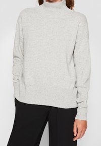 Helles graues gestricktes Rollkragensweatshirt mit lockerer Passform, gerippten Bündchen und Saum. Weiche Textur mit dezenten Sprenkeln.
